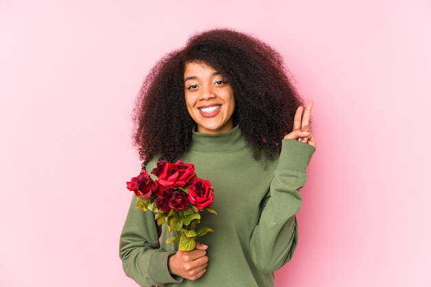 Jovem mulher afro segurando rosas isoladas Jovem mulher afro segurando uma rosa mostrando o número dois com os dedos.