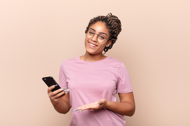 Jovem mulher afro sorrindo alegremente, sentindo-se feliz e mostrando um conceito no espaço da cópia com a palma da mão.