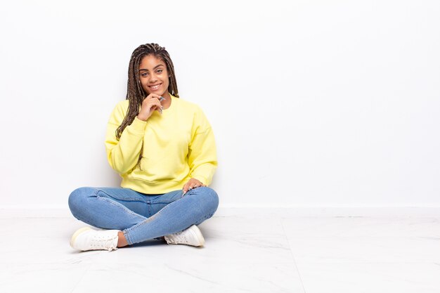 Jovem mulher afro sorrindo, curtindo a vida, sentindo-se feliz, simpática, satisfeita e despreocupada com a mão no queixo