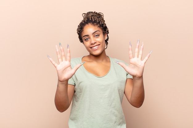 Jovem mulher afro sorrindo e parecendo amigável, mostrando o número dez ou décimo com a mão para a frente, em contagem regressiva