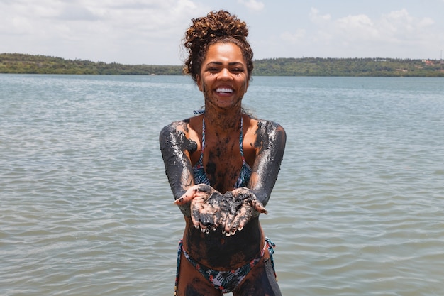 Jovem mulher afro tomando banho em argila natural no rio.