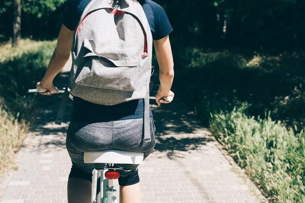 Jovem mulher anda de bicicleta com uma mochila no verão