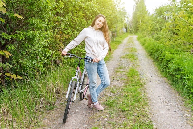 Jovem mulher andando de bicicleta no parque da cidade de verão ao ar livre. Pessoas ativas. Garota hipster relaxa e motociclista. Andar de bicicleta para o trabalho no dia de verão. Conceito de estilo de vida de bicicleta e ecologia