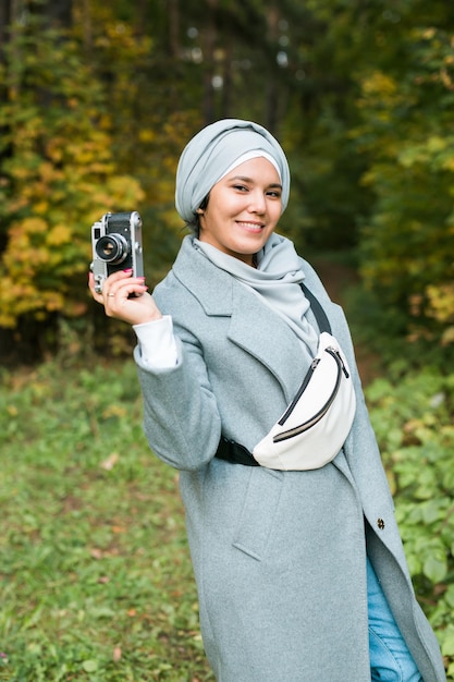 Jovem mulher árabe com lenço na cabeça hijab fotografando com um smartphone no parque.