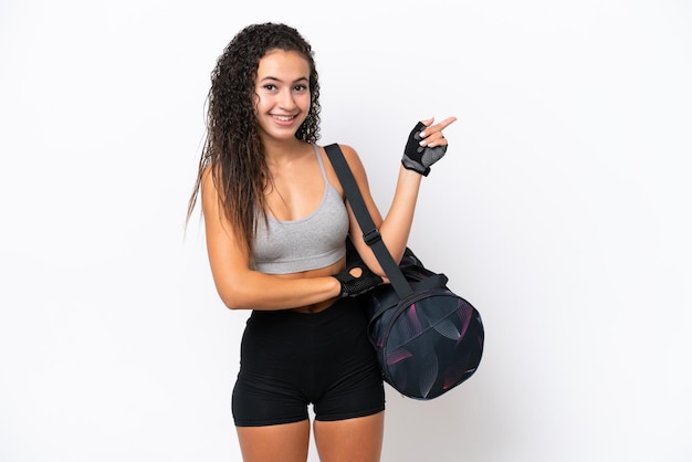 Jovem mulher árabe esportiva com bolsa esportiva isolada no fundo branco, apontando o dedo para o lado