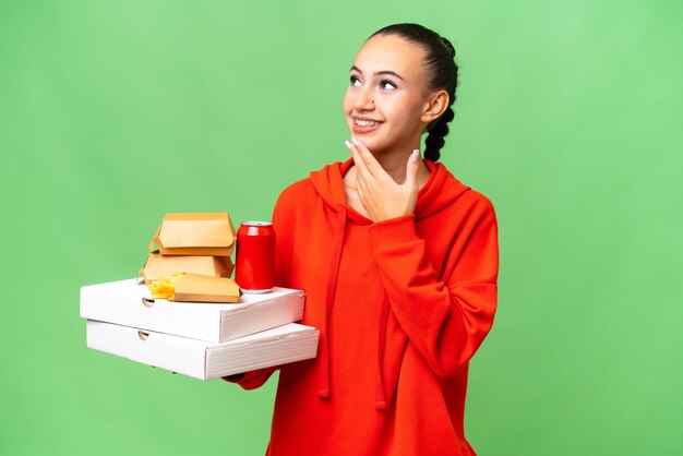 Jovem mulher árabe segurando fast-food sobre fundo isolado, olhando para cima enquanto sorri