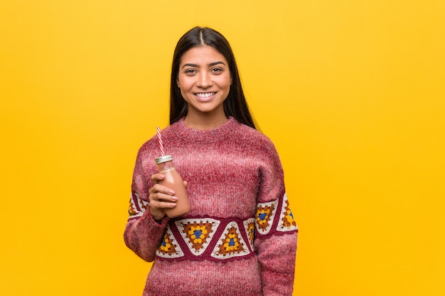 Jovem mulher árabe segurando um batido feliz, sorridente e alegre.