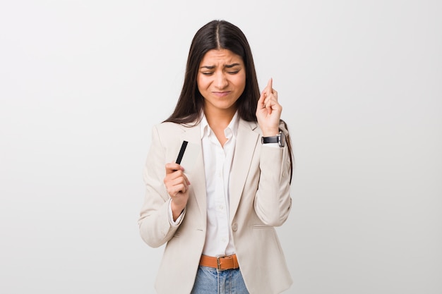Jovem mulher árabe segurando um cartão de crédito, cruzando os dedos por ter sorte
