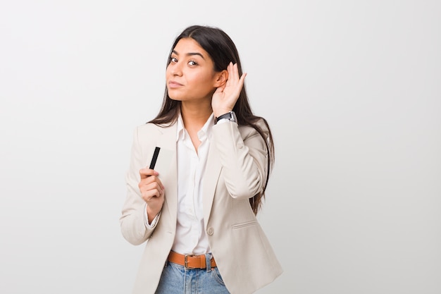 Jovem mulher árabe segurando um cartão de crédito, tentando ouvir uma fofoca.