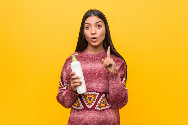 Jovem mulher árabe segurando um frasco de creme, tendo uma ótima idéia, de criatividade.