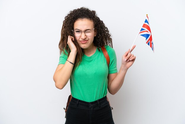 Jovem mulher árabe segurando uma bandeira do Reino Unido isolada em fundo branco frustrada e cobrindo os ouvidos