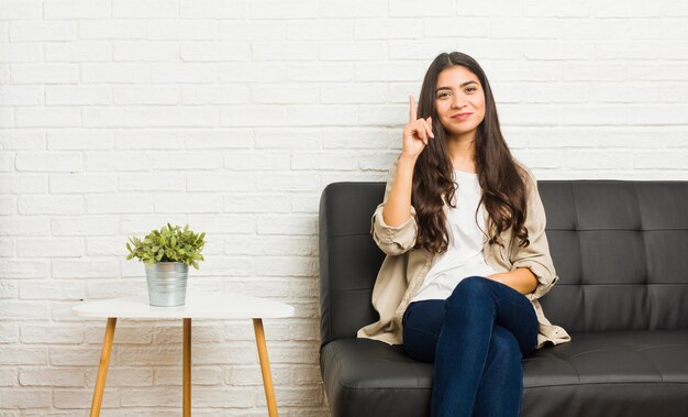 Jovem mulher árabe sentada no sofá, mostrando o número um com o dedo.