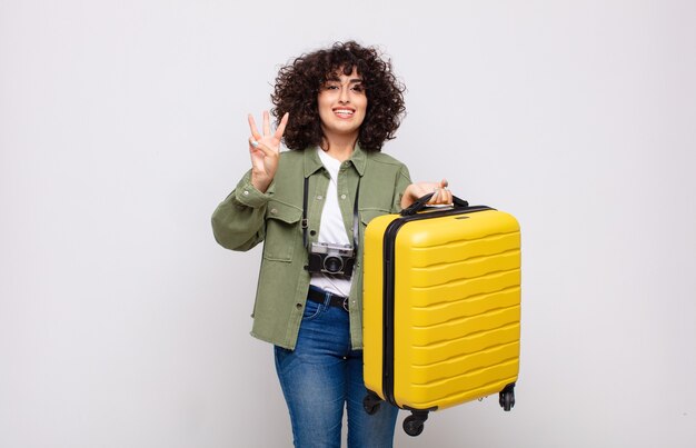 Foto jovem mulher árabe sorrindo e parecendo amigável, mostrando o número três ou terceiro com a mão para a frente, conceito de viagem em contagem regressiva
