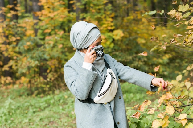 Jovem mulher árabe usando lenço na cabeça hijab fotografando com um smartphone no parque. Menina muçulmana moderna