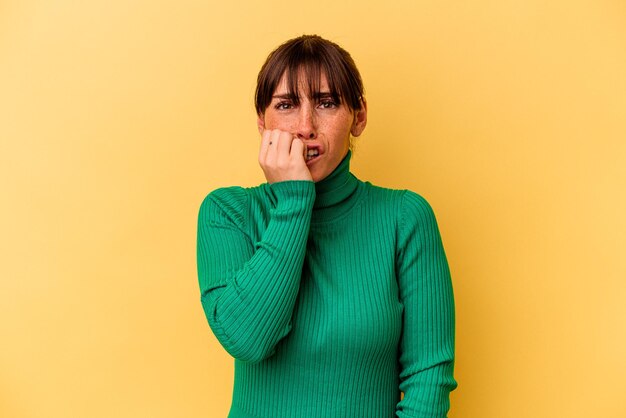 Jovem mulher argentina isolada em fundo amarelo, roer unhas, nervoso e muito ansioso.