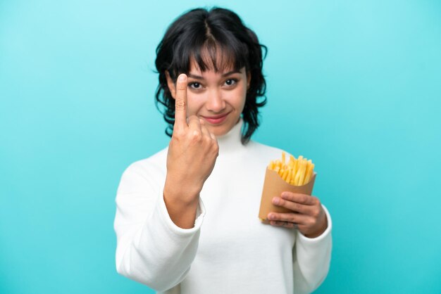 Jovem mulher argentina segurando batatas fritas isoladas em fundo azul, fazendo o próximo gesto