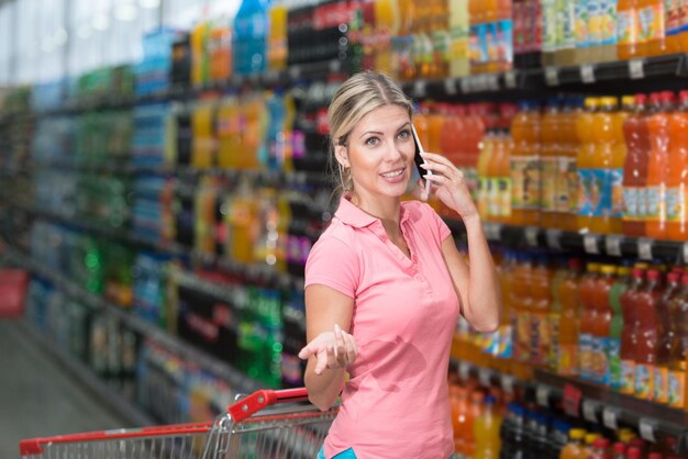 Jovem mulher às compras no supermercado enquanto usa o smartphone na loja