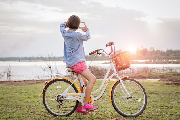 Jovem, mulher asian, ligado, bicicleta olha, em, mão, quadro, vista, pôr do sol