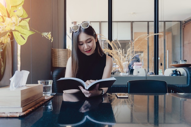 Jovem mulher asiática, aproveitando o livro de leitura enquanto está sentado em casa