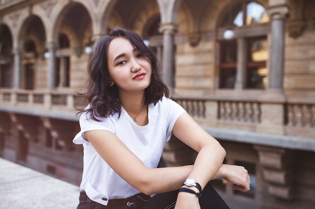 Jovem mulher asiática atraente em uma camiseta branca e calça jeans preta no prédio histórico