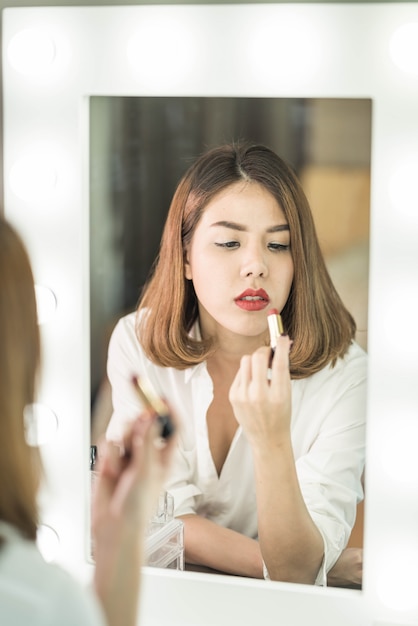 Jovem mulher asiática bonita fazendo maquiagem perto de espelho