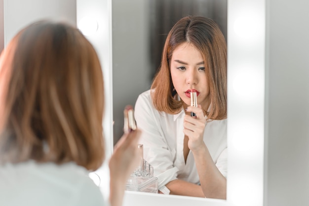 Jovem mulher asiática bonita fazendo maquiagem perto de espelho