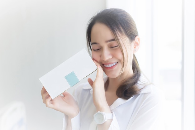 Jovem mulher asiática bonita tem a caixa branca (a caixa de presente) nas mãos com uma cara feliz.