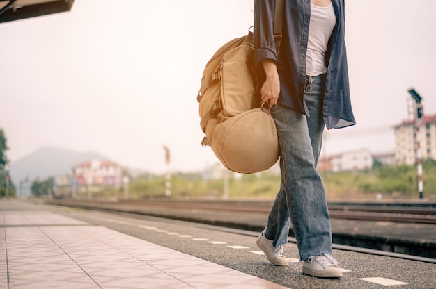 Jovem mulher asiática caminhando e espera o trem na plataforma ferroviária. Conceito de turismo, viagens e lazer.