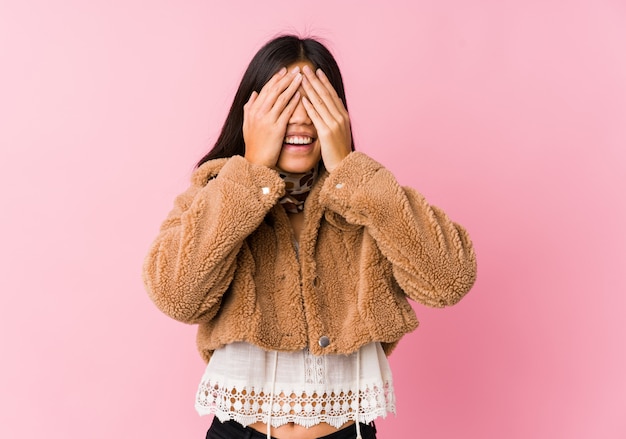 Jovem mulher asiática cobre os olhos com as mãos, sorri amplamente esperando por uma surpresa.