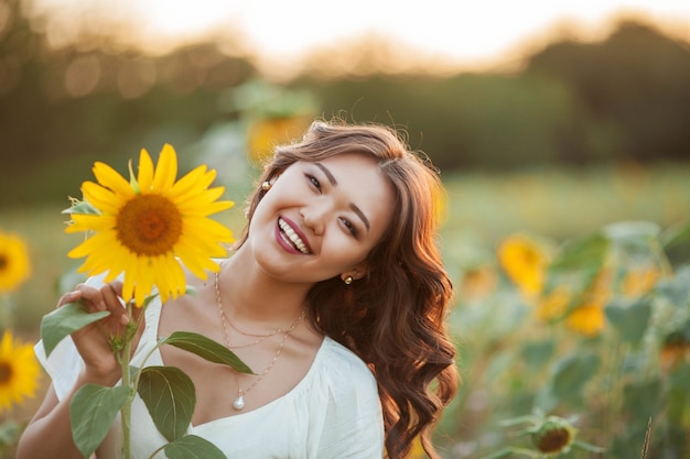 Jovem mulher asiática com cabelo encaracolado em um campo de girassóis ao pôr do sol. retrato de uma jovem mulher asiática bonita ao sol. verão.