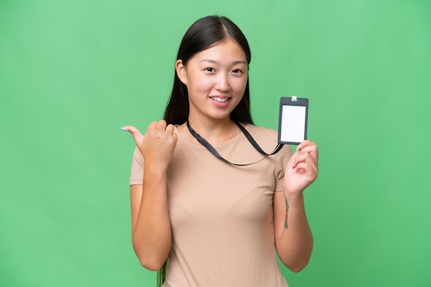 Jovem mulher asiática com carteira de identidade sobre fundo isolado, apontando para o lado para apresentar um produto