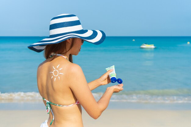 Jovem mulher asiática com forma de sol no ombro aplicar protetor solar na mão dela. Verão no conceito de praia.