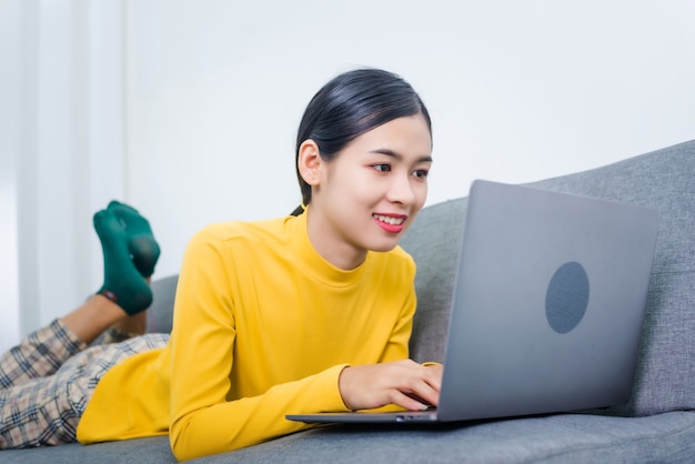 Jovem mulher asiática com laptop deitado no sofá