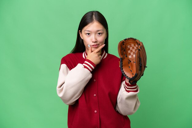 Jovem mulher asiática com luva de beisebol sobre fundo isolado pensando