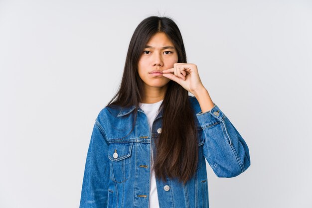 Jovem mulher asiática com os dedos nos lábios, mantendo um segredo.