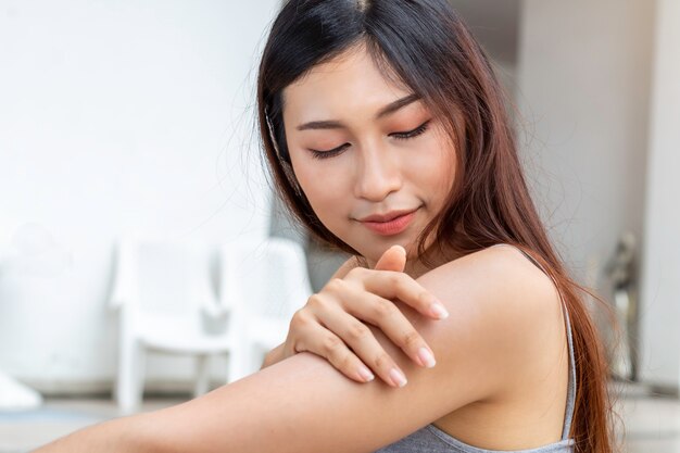 Jovem mulher asiática com pele saudável, aplicar protetor solar Uv proteger ao ombro.