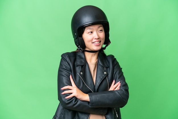 Jovem mulher asiática com um capacete de motocicleta sobre fundo croma isolado feliz e sorridente