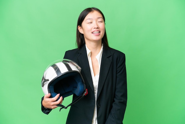 Jovem mulher asiática com um capacete de motocicleta sobre fundo croma isolado rindo