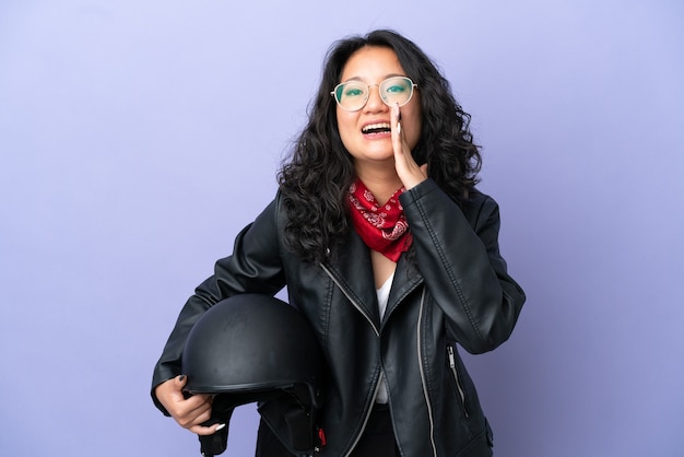 Jovem mulher asiática com um capacete de motociclista isolada em um fundo roxo gritando com a boca bem aberta