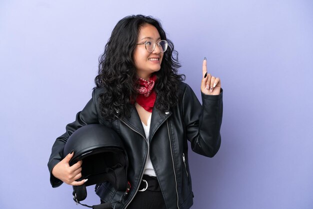 Jovem mulher asiática com um capacete de motociclista isolado em um fundo roxo apontando para uma ótima ideia