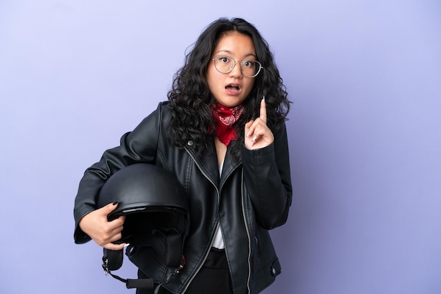 Jovem mulher asiática com um capacete de motociclista isolado em um fundo roxo com a intenção de perceber a solução enquanto levanta um dedo