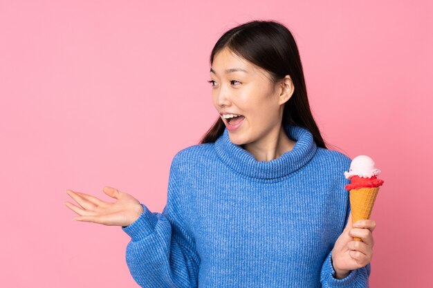 Jovem mulher asiática com um sorvete de corneta na parede rosa com expressão facial de surpresa
