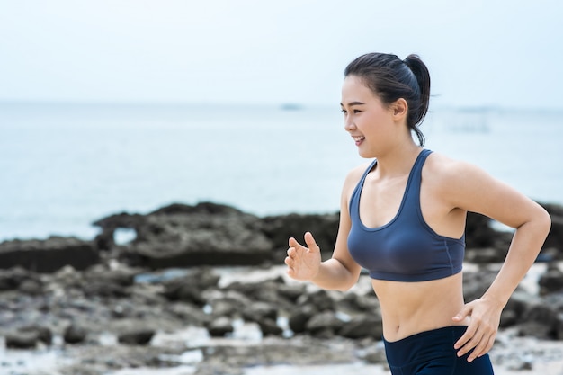 Jovem mulher asiática correndo na praia. Treino de corrida de menina na beira-mar