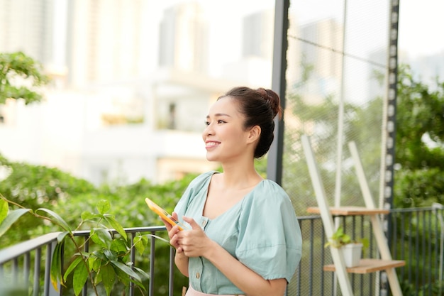 Jovem mulher asiática curtindo a natureza e usando o telefone na varanda