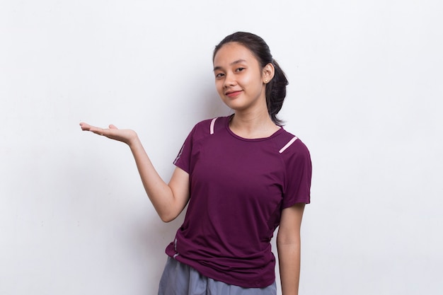 Jovem mulher asiática desportiva apontando o dedo em um espaço vazio no fundo branco