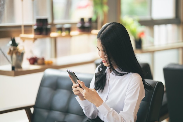 Jovem mulher asiática digitando mensagem de texto em um telefone inteligente em um café