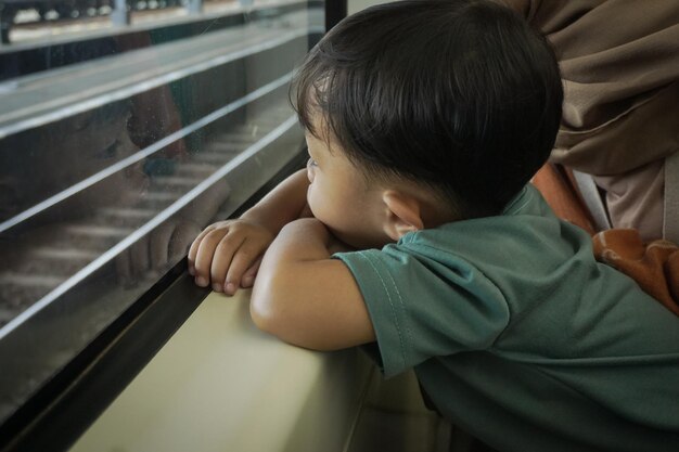 Jovem mulher asiática em hijab e seu filho estão conversando e olhando pela janela dentro do trem