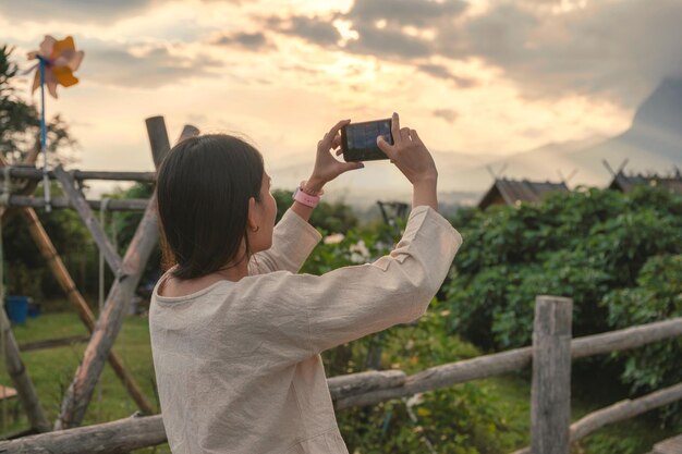 Jovem mulher asiática em pano casual tirando uma foto com smartphone na colina na floresta tropical