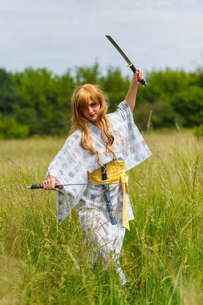 Jovem mulher asiática em quimono tradicional treina técnicas de luta com espada katana ao ar livre, garota guerreira samurai