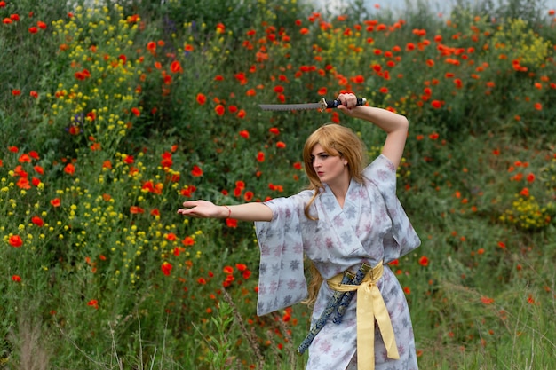 Jovem mulher asiática em quimono tradicional treina técnicas de luta com espada katana nas colinas com papoilas vermelhas, garota guerreira samurai